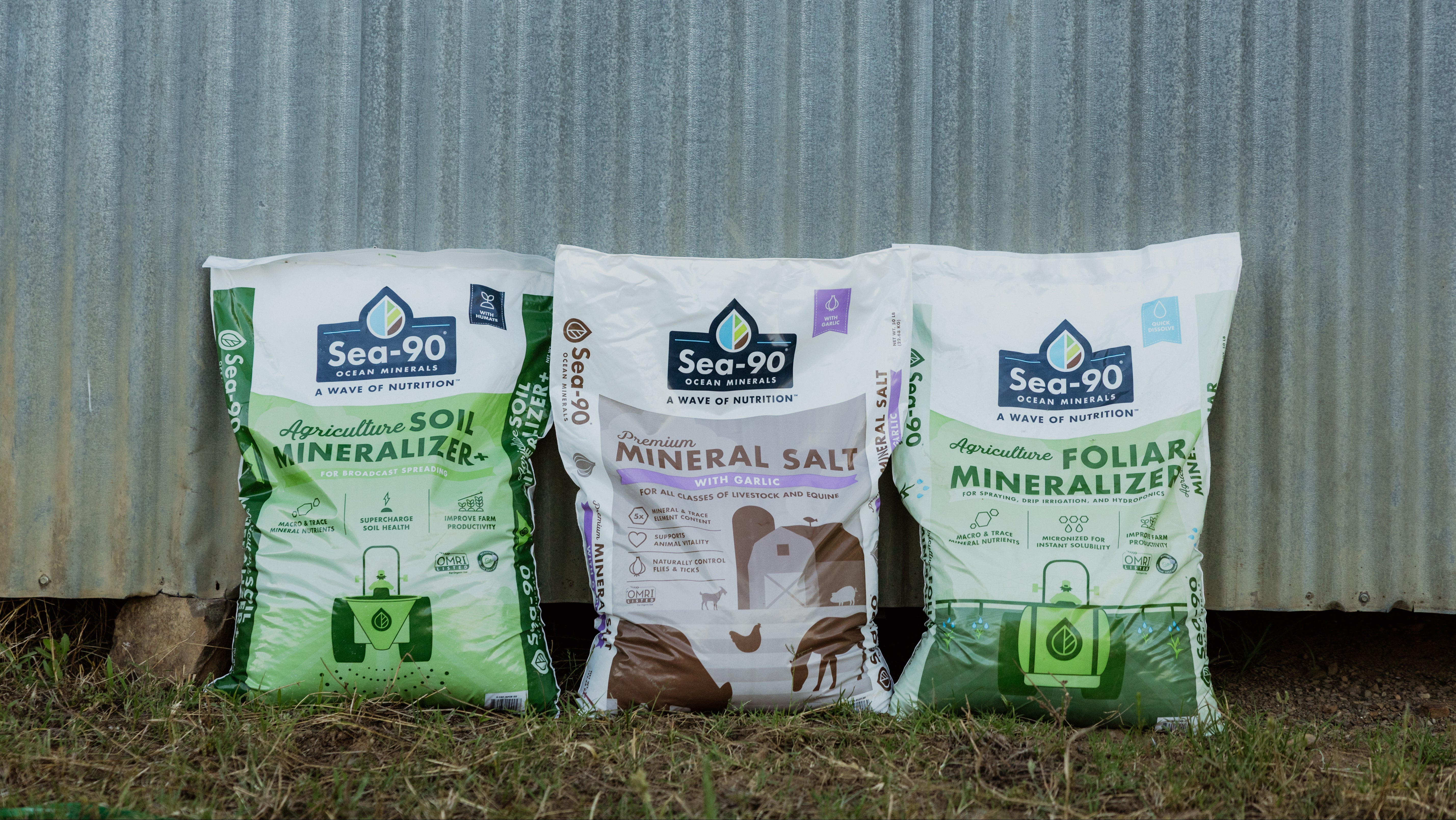 Three bags of Sea-90 agricultural products against a corrugated metal background.